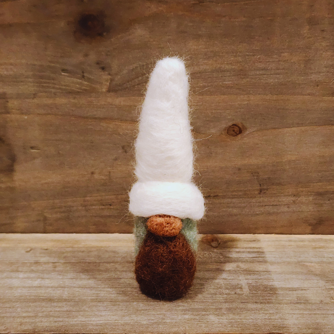 A handmade needle-felted gnome with an aqua body, a tall white hat, a brown beard, and an orange nose, standing centered against a rustic wooden background.