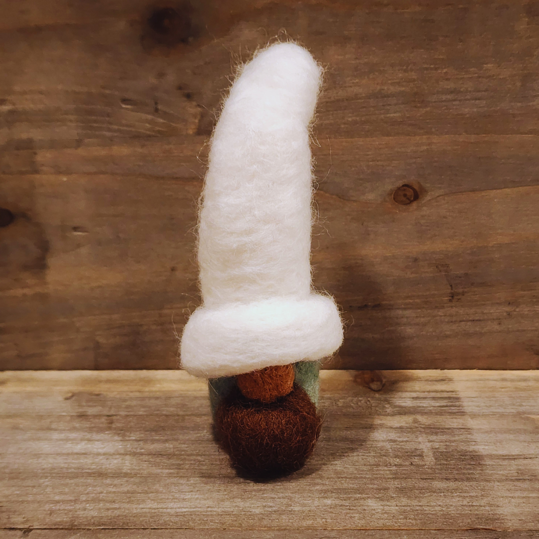 A handmade needle-felted gnome with an aqua body, a tall white hat, a brown beard, and an orange nose, viewed from a slightly angled perspective against a rustic wooden background.