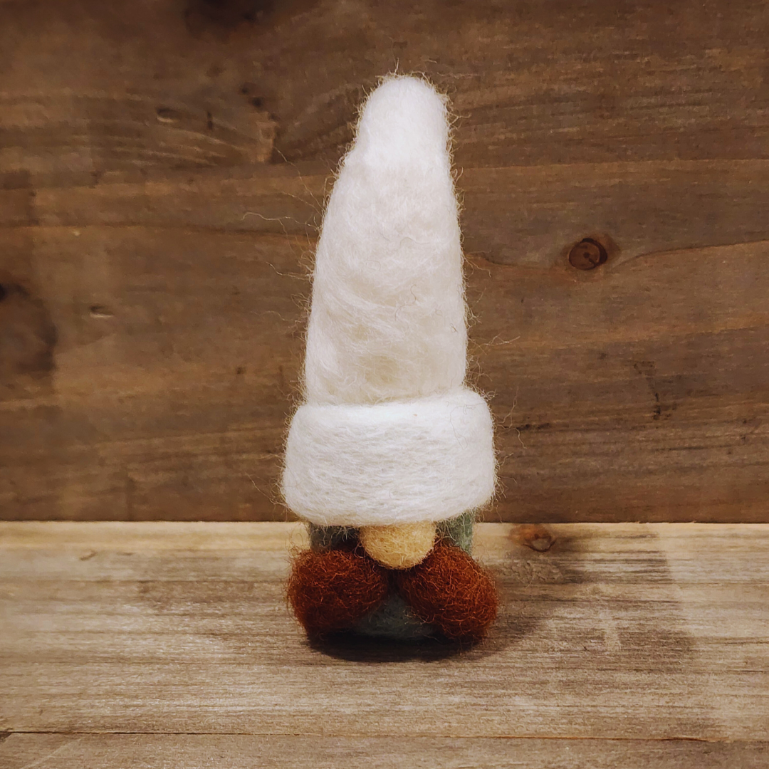 A handmade needle-felted gnome with an aqua body, a tall white hat, a brown mustache, and a light-colored nose, standing centered against a rustic wooden background.