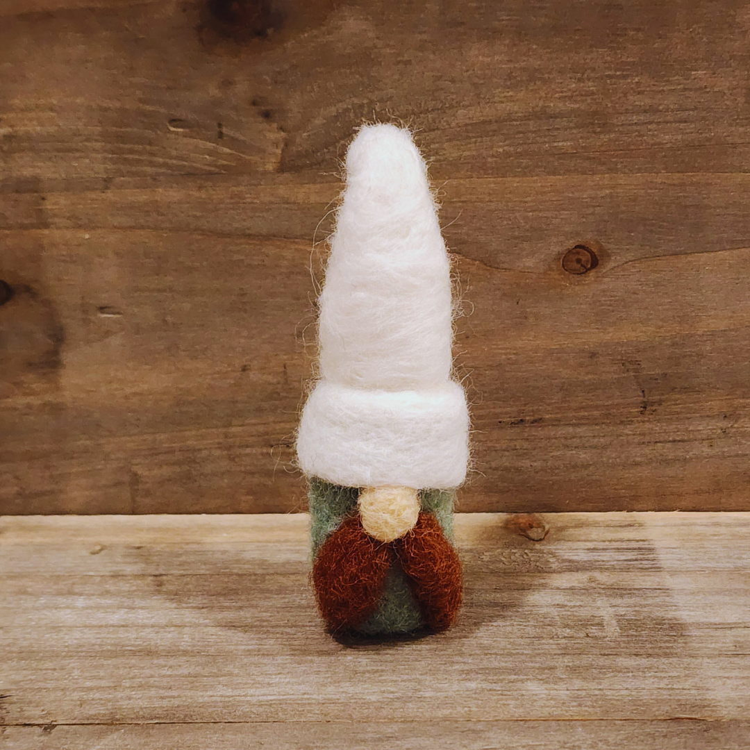 A handmade needle-felted gnome with an aqua body, a tall white hat, a brown mustache, and a light-colored nose, standing centered against a rustic wooden background.