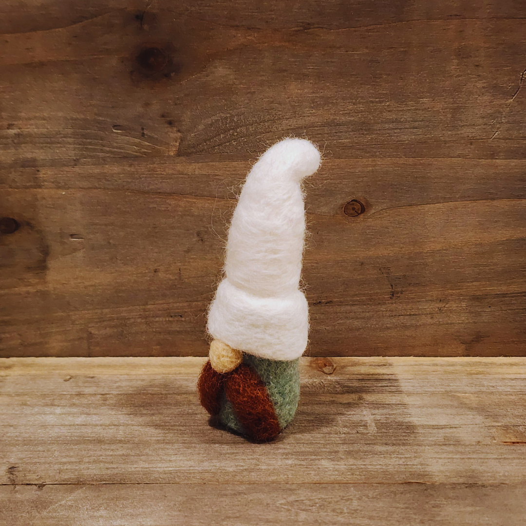 A handmade needle-felted gnome with an aqua body, a tall white hat, a brown mustache, and a light-colored nose, viewed from a slightly angled perspective against a rustic wooden background.