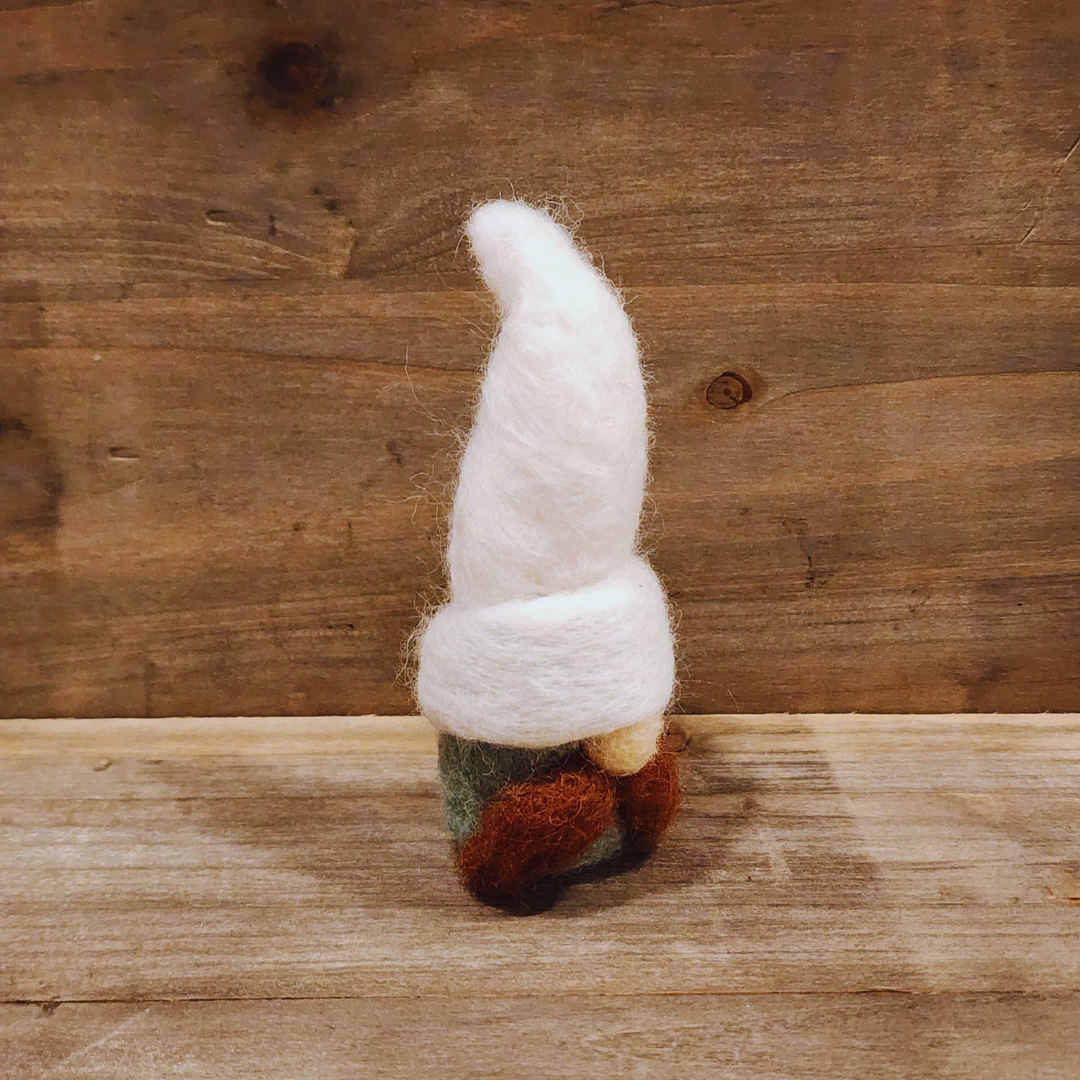 A handmade needle-felted gnome with an aqua body, a tall white hat, a brown beard, and an orange nose, viewed from a slightly angled perspective against a rustic wooden background.