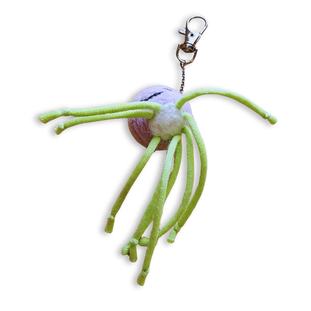 A handmade jellyfish charm is shown from the underside, revealing a round, pink and gray body with bright green rope-like tentacles and a silver clip-on keychain.
