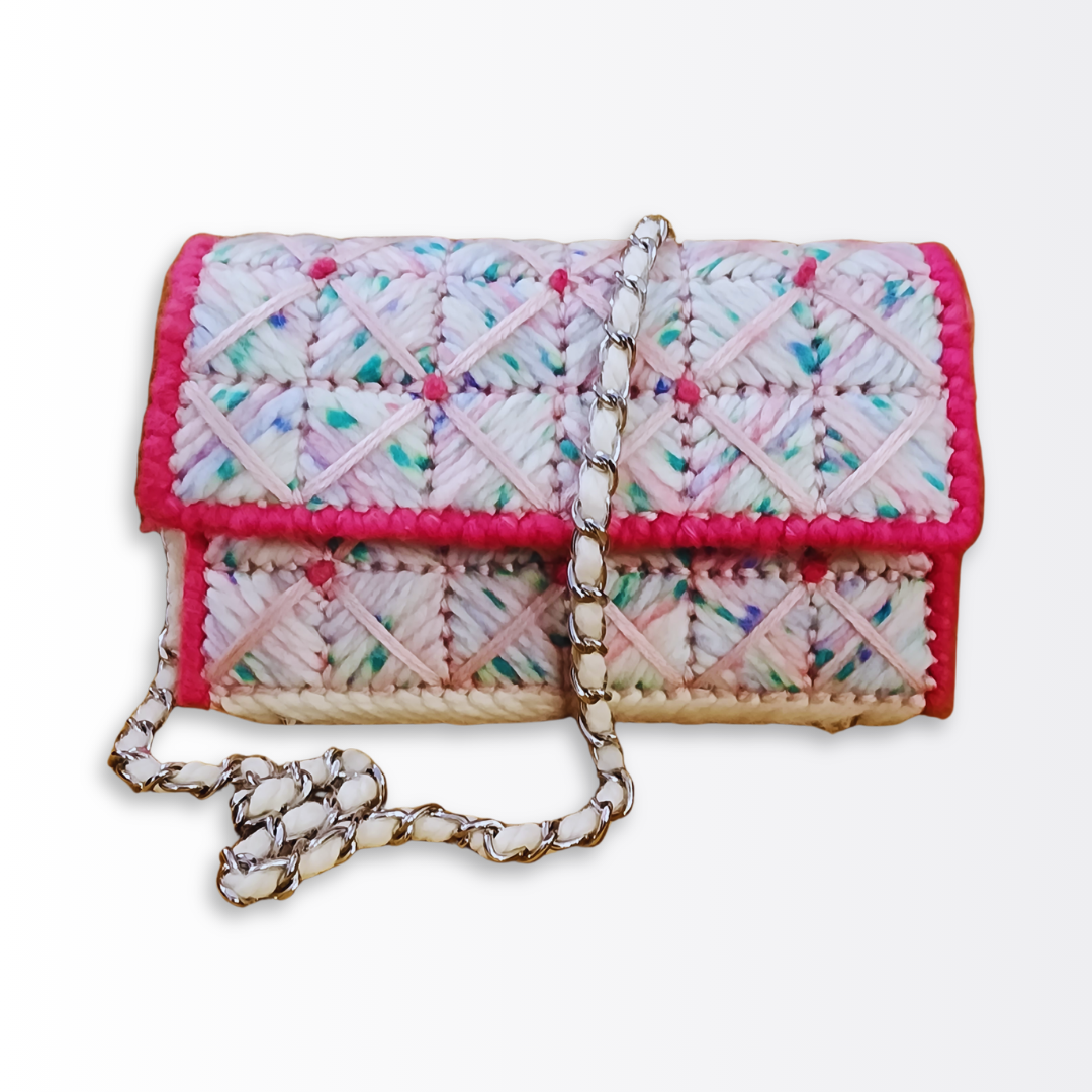 Front-facing view of the Strawberry Shortcake Bargello Mini Clutch highlighting the pink and white geometric checkered pattern, crisscross yarn overlay, and the silver chain strap with white yarn woven through the links.