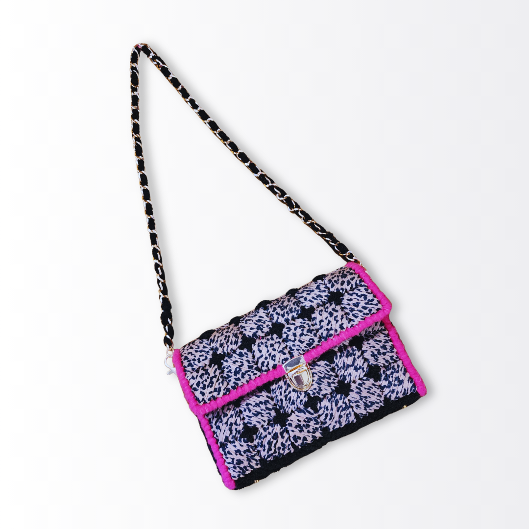 Angled view of the Leopard Mini Clutch with the 26-inch gold chain strap extended, showcasing the black chenille yarn woven through the links.