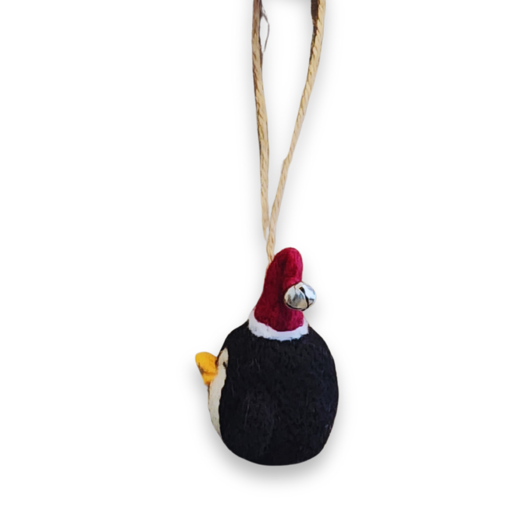 A lower perspective of the penguin ornament, showing the orange beak, the black wool body, and the red and white Santa hat with the bell.