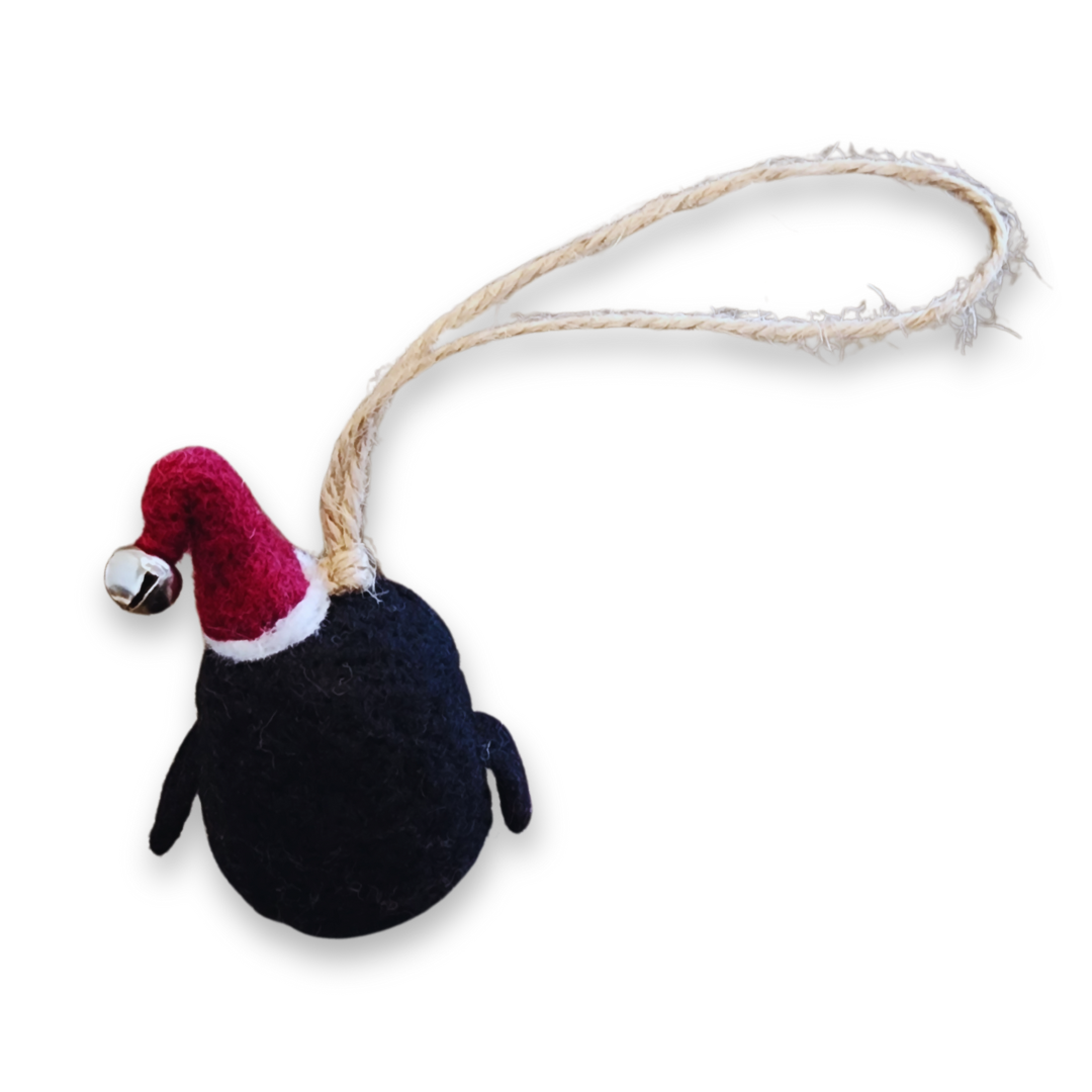 A side view of the felted penguin ornament, highlighting the thick jute string loop and the small silver bell on the red hat.