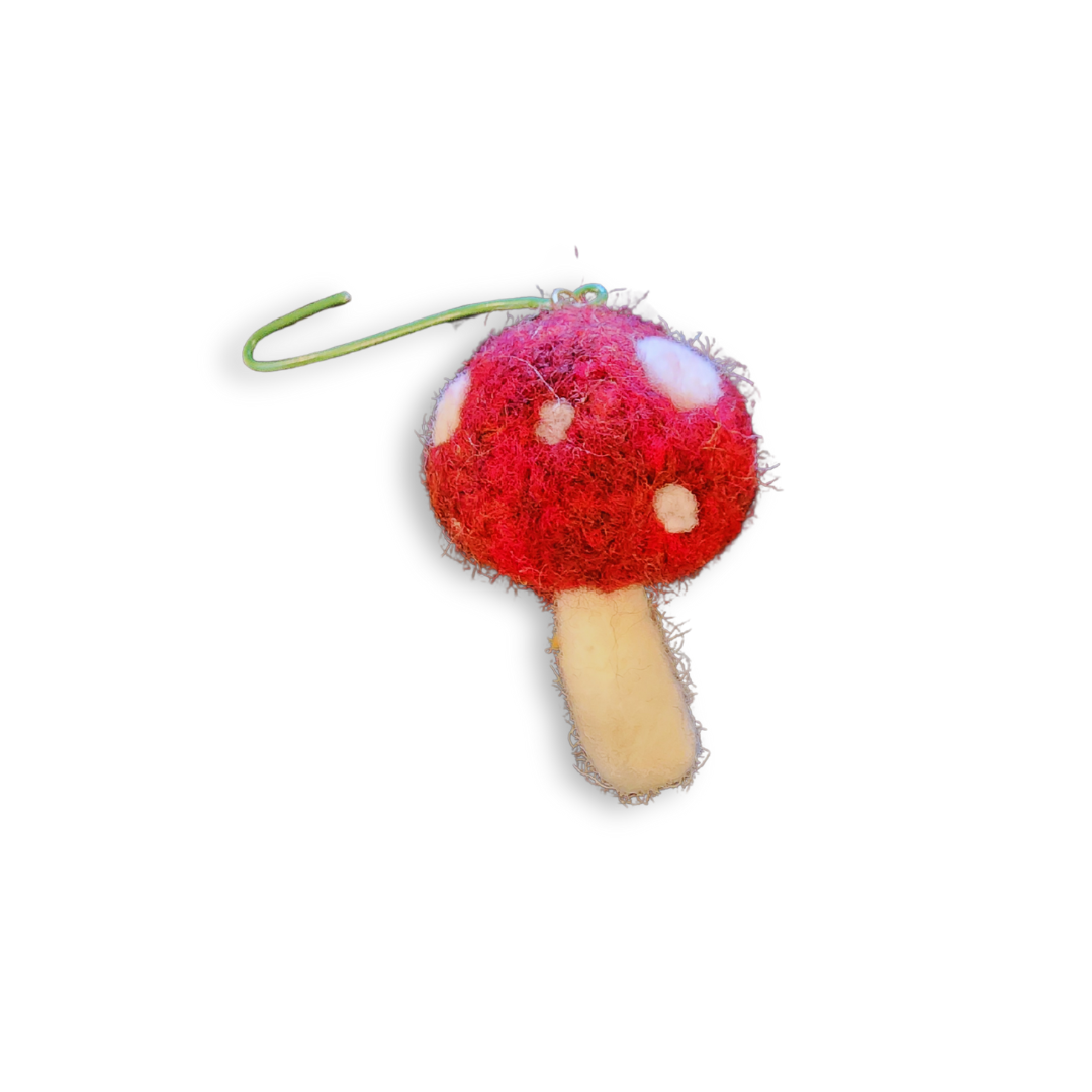 A close-up studio shot of a tiny, needle-felted red and white toadstool ornament, showing the fuzzy texture of the wool. A green wire hanger is visible at the top.
