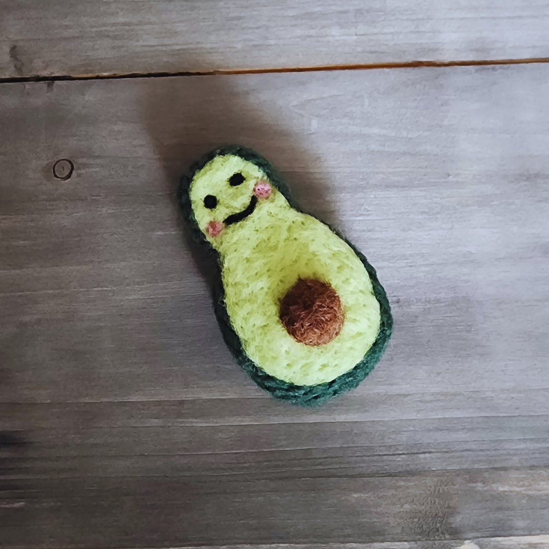 A close-up, slightly overhead shot of the handmade avocado cat toy lying on a rustic grey wooden surface.