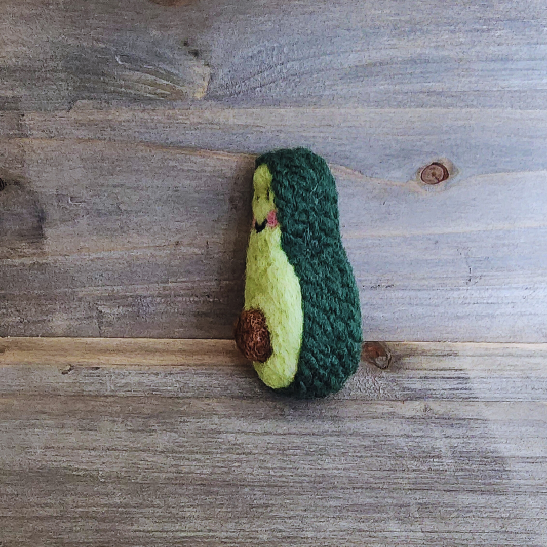 A side profile view of the needle-felted avocado toy, highlighting the thick, textured dark green "skin" made of felted yarn.