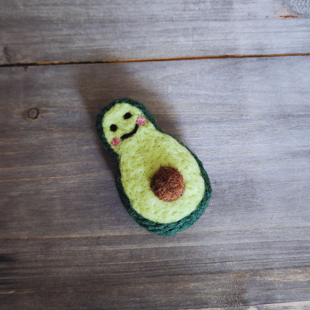 A high-angle shot of the avocado toy resting on a wooden plank, showing the fuzzy texture of the light green wool interior.