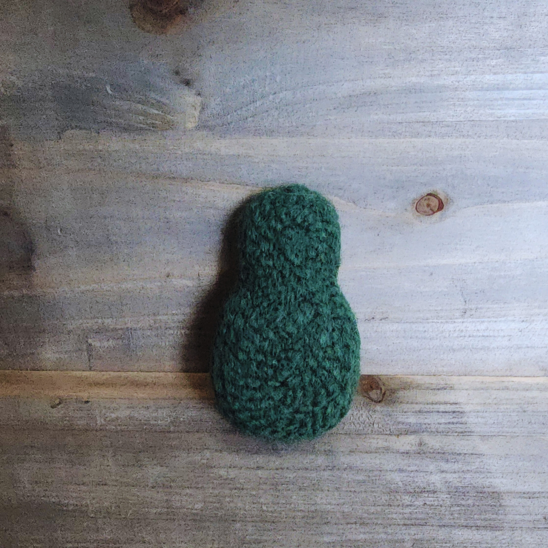 The back view of the avocado toy, showing the solid, dark green felted acrylic and wool yarn exterior.