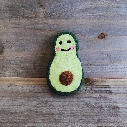A centered, front-facing shot of the avocado toy standing upright against a wooden backdrop, showcasing its symmetrical shape and smiling face.