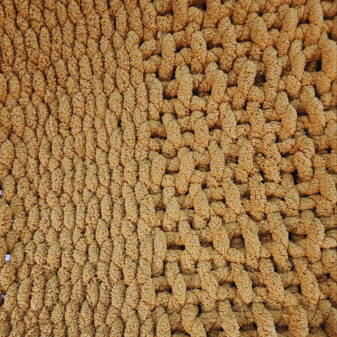 A close-up overhead view of a handmade hand-crocheted blanket, showing alternating rows of textured single stitch and basket weave stitch patterns in a sunset yellow color.