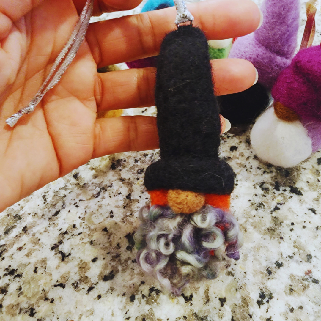 Close-up of a hand holding a gnome ornament with a tall black hat and fluffy, curly gray and purple beard.
