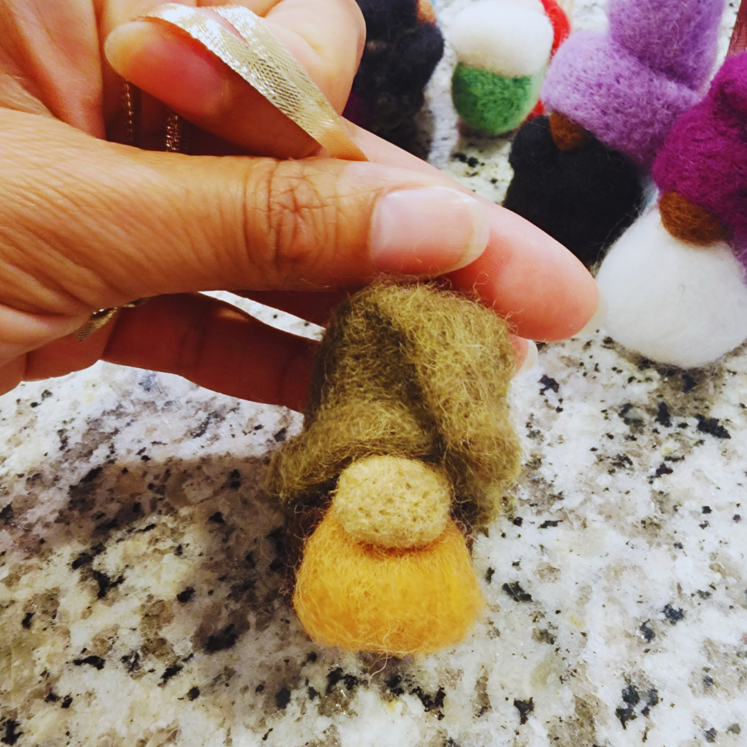 Close-up of a hand holding a gnome ornament with a slouchy green hat, a small beige nose, and a fluffy yellow body.
