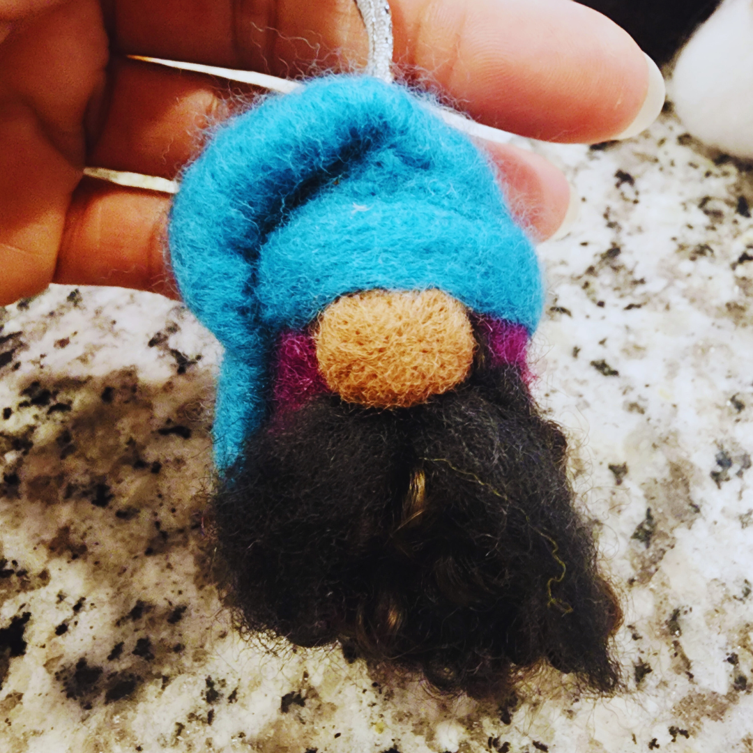 Close-up of a hand holding a gnome ornament featuring a bright blue hat, a small brown nose, and a dark, shaggy beard.