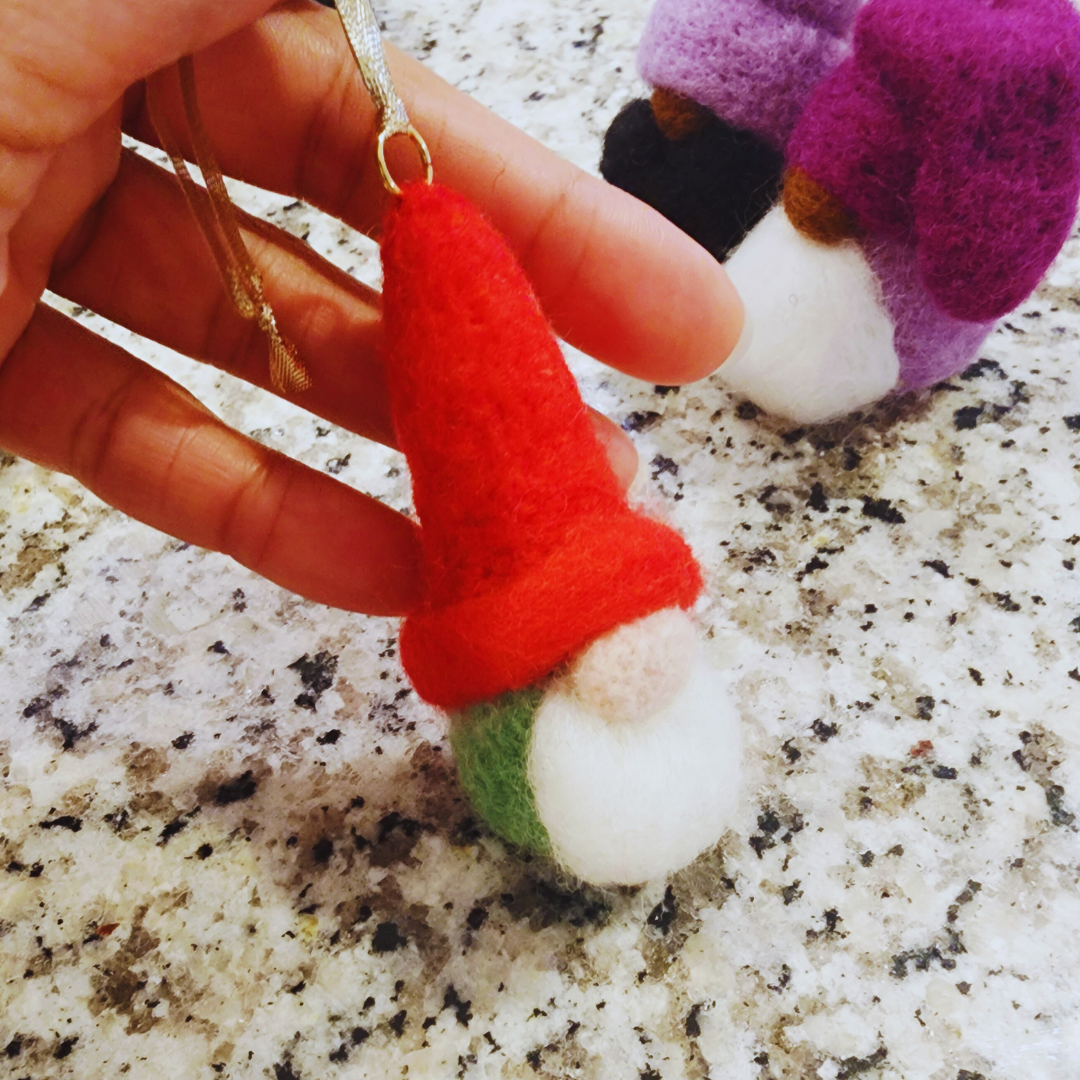 Close-up of a hand holding a gnome ornament with a bright red conical hat, a white beard, and a green and white lower body.