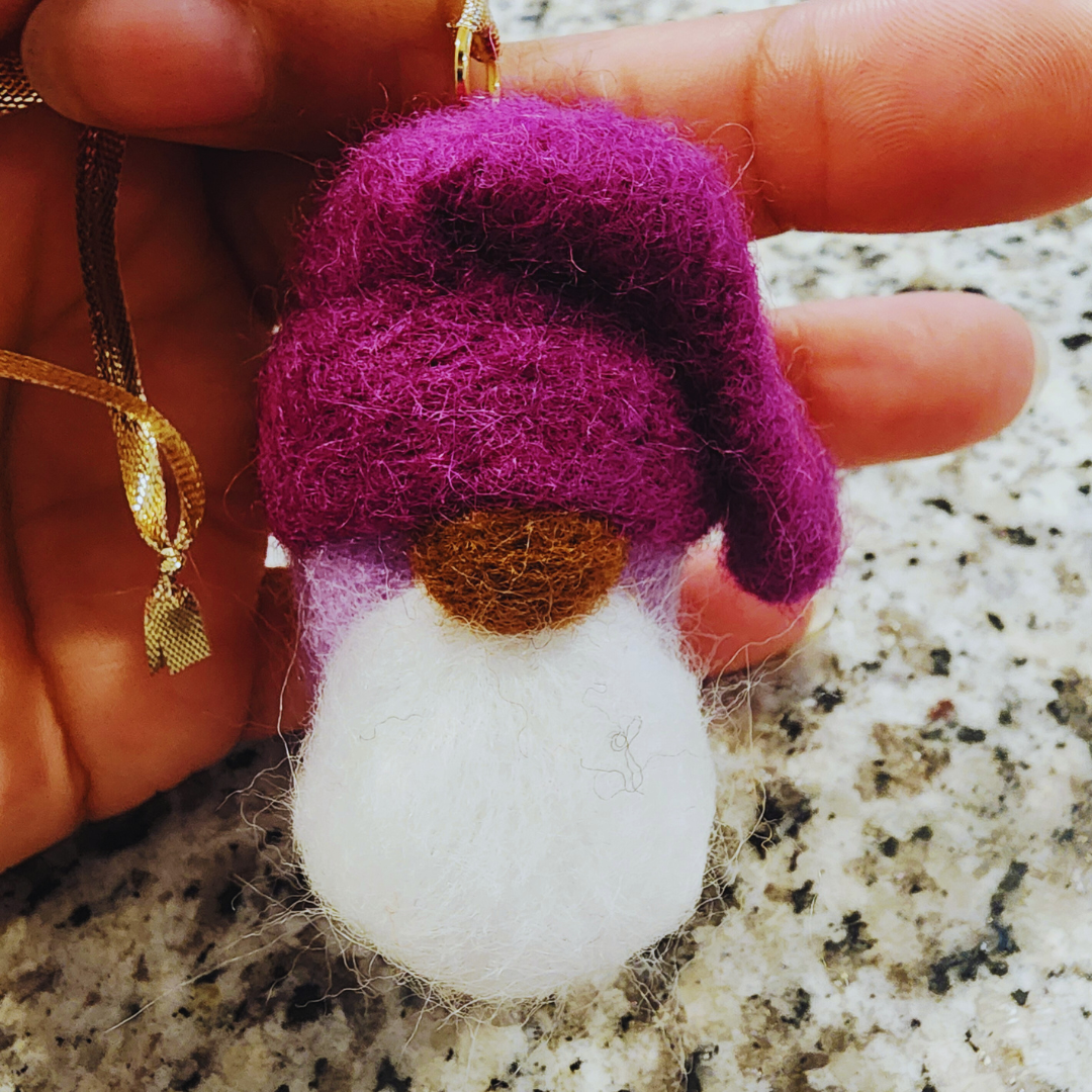 Close-up of a hand holding a gnome ornament with a vibrant magenta-purple hat, a brown nose, and a large white spherical beard/body.