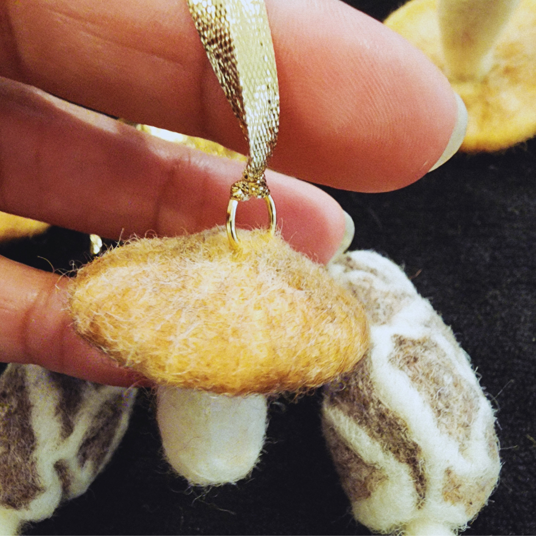 Extreme close-up of the fuzzy orange cap of a round, needle-felted mushroom ornament, showing the texture of the wool and the gold hanging loop.