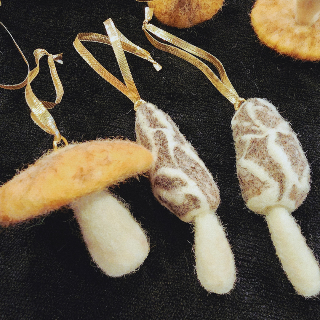 Close-up of one round, orange-capped mushroom ornament next to two patterned morel mushroom ornaments, showing their different shapes and textures.