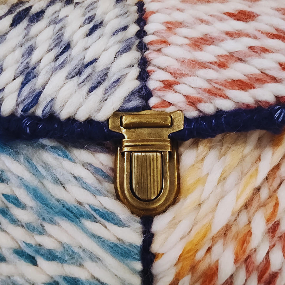 Macro shot of the ornate bronze push-lock clasp on a hand-embroidered patchwork exterior, demonstrating the bag's luxury fiber art quality.