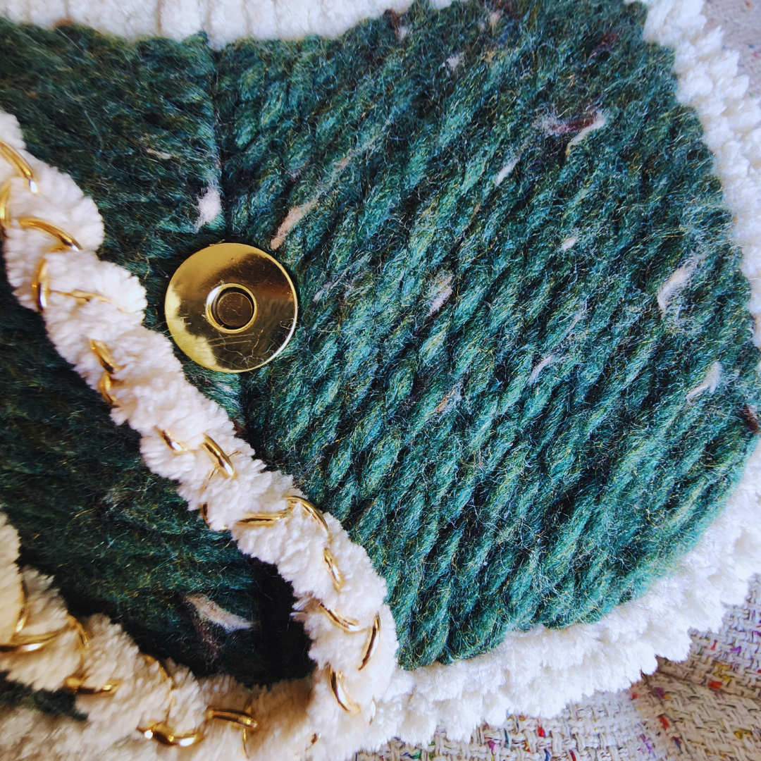 A close-up of the magnetic clasp on the bag's flap, showing the gold metal hardware against the deep green embroidered yarn and the thick white chenille trim.