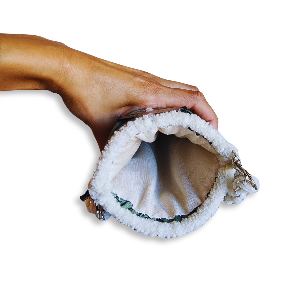 A hand opens the top of the green phone purse, showing the fluffy white chenille trim and the cream-colored fabric lining inside.