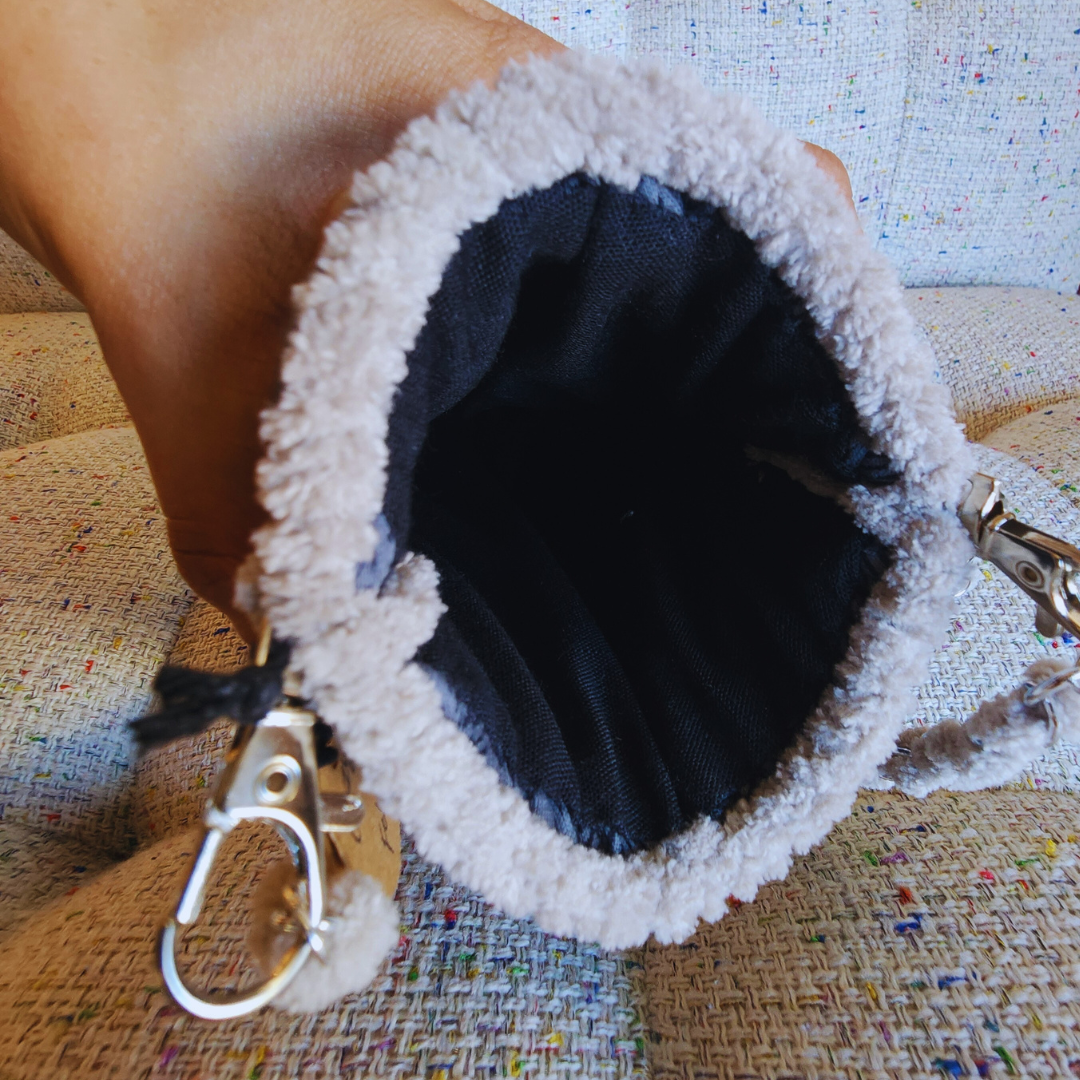 A hand holds the top opening of the gray embroidered phone purse, showing the dark, hand-sewn lining inside and the fuzzy beige chenille edge.