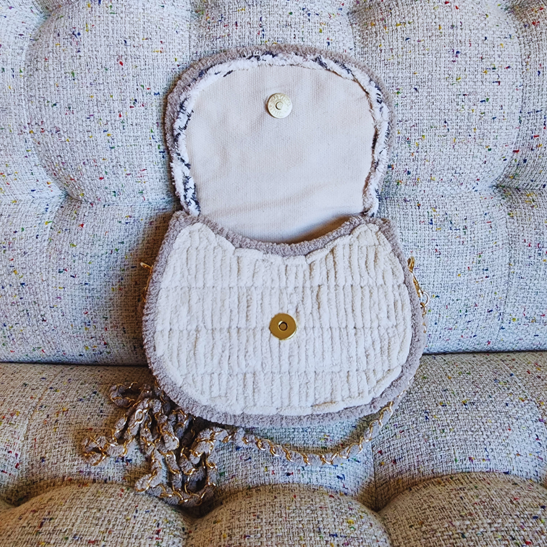 The saddlebag is shown open, revealing the secure magnetic clasp closure on the cream-colored lining and the main body of the purse.