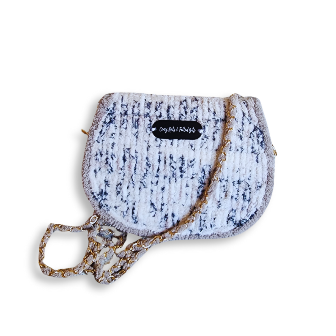 A front-facing view of the small, rounded saddlebag, showing the white and speckled blue/black chenille with a small branded tag on the flap.