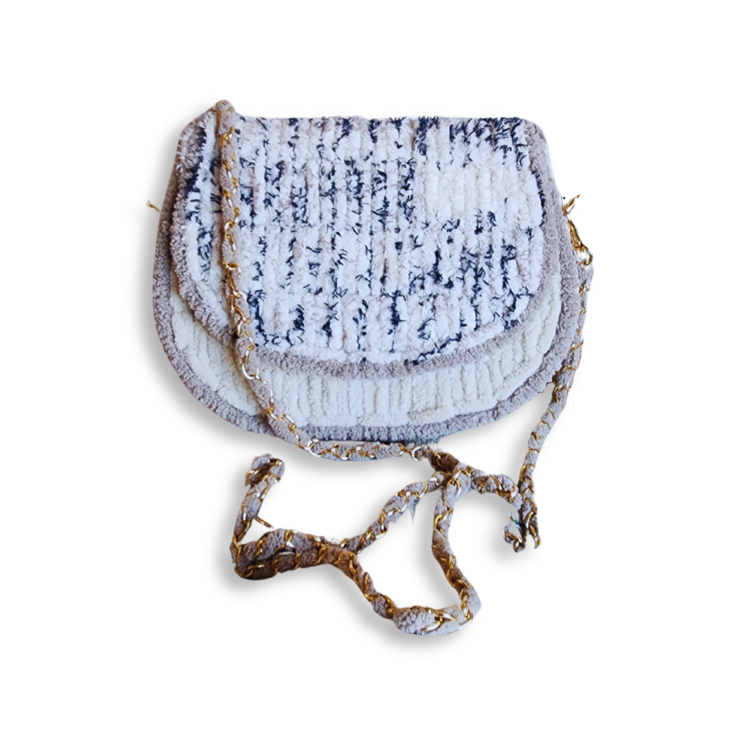 An overhead view of the closed saddlebag, showcasing the curved bottom and the gold chain strap woven with beige yarn.