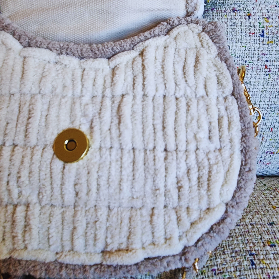 A close-up of the underside of the saddlebag's flap, showing the plush cream-colored chenille texture and the magnetic clasp closure mechanism.