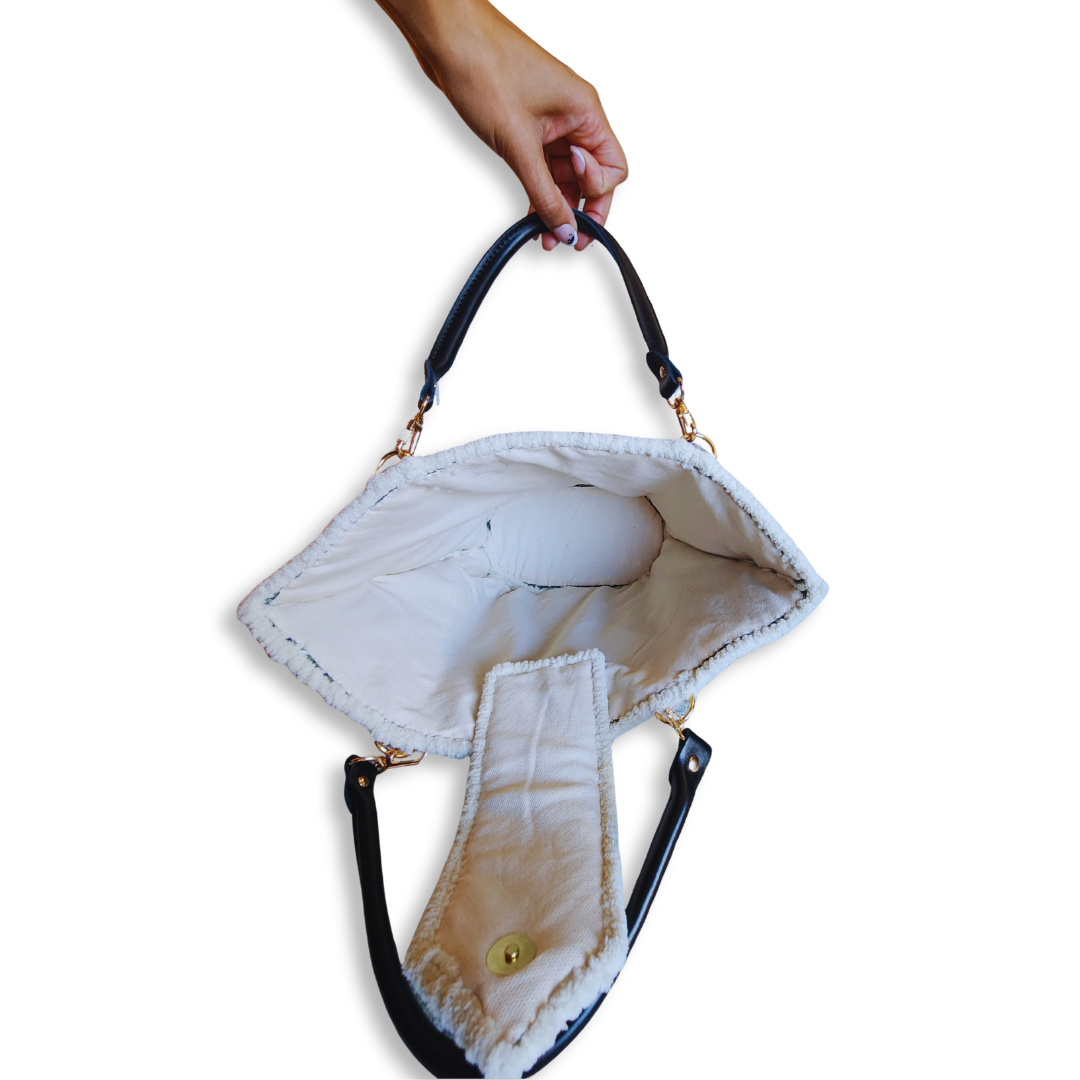 A hand holds the tote bag open from an overhead perspective, displaying the interior space and the soft texture of the white lining and trim.