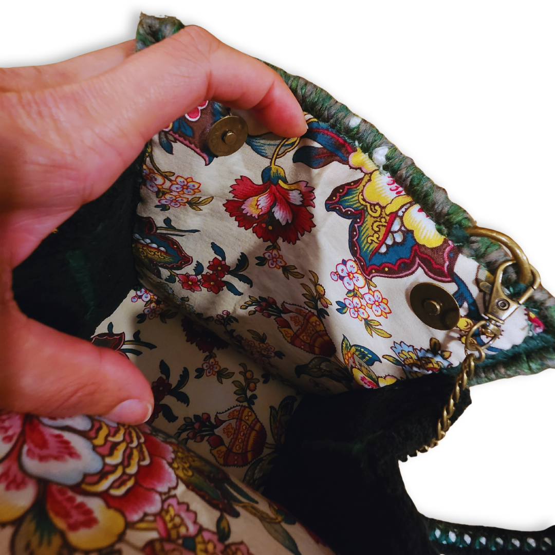 A hand opens the bag, revealing the vibrant, multicolor floral patterned fabric lining, the bronze magnetic closure, and the inner construction.