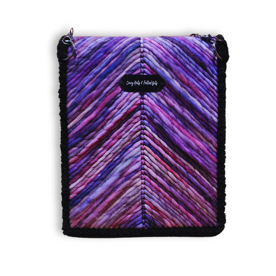 A structured, one-of-a-kind embroidered shoulder bag made with hand-dyed Merino wool yarn in stunning lavender ombre colors. The bag has a black chenille border and a small black tag.