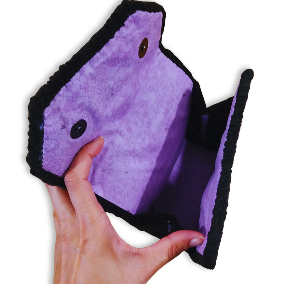 A hand opens the bag, revealing the light purple floral patterned fabric lining and the black magnetic snap closure hardware.