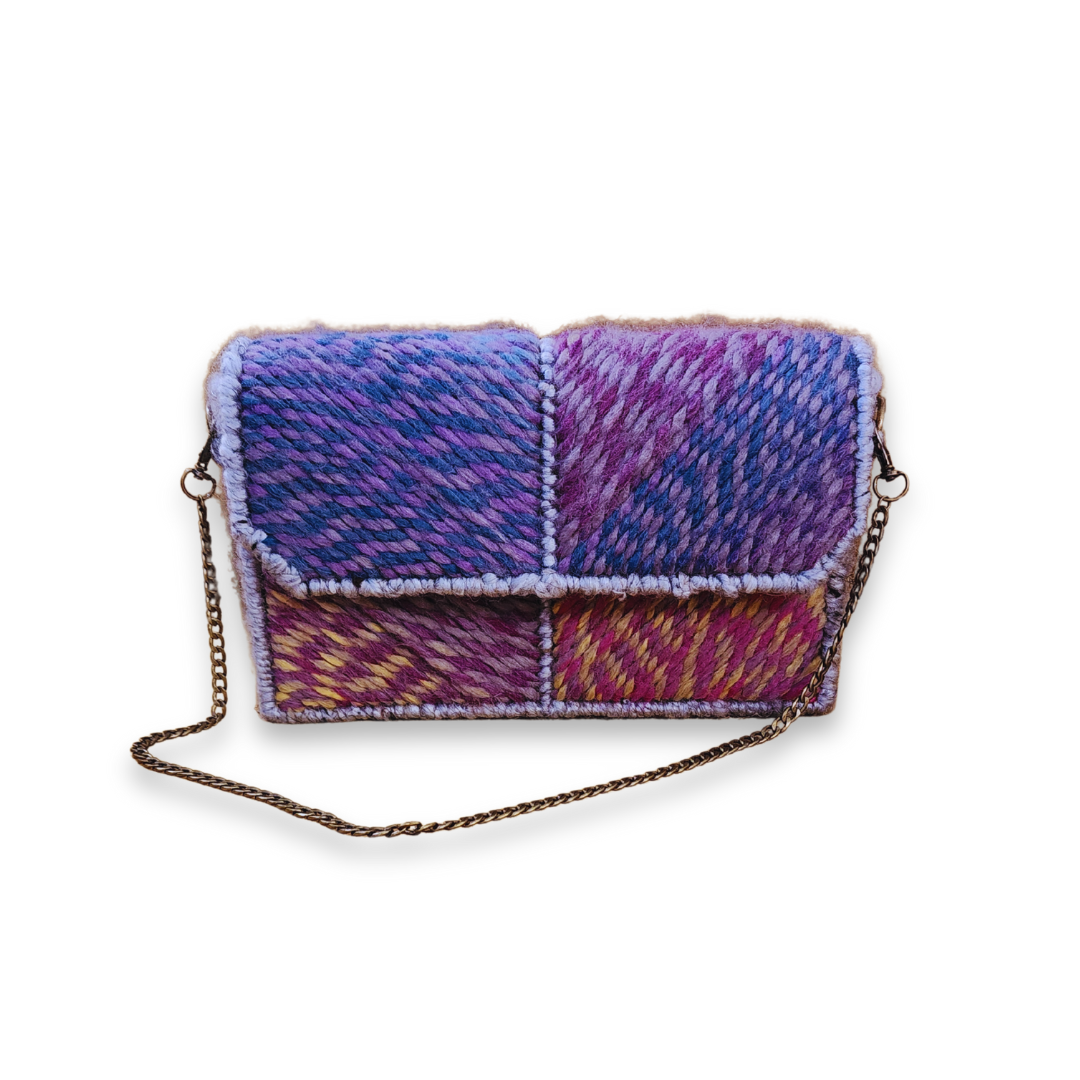 A structured, one-of-a-kind embroidered clutch/shoulder bag featuring a four-panel patchwork design in blue, purple, pink, and yellow yarn, with a brass chain strap visible below.