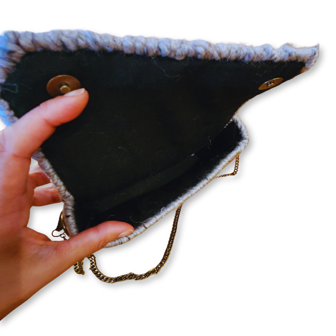 A close-up view of the open clutch, detailing the dark inner lining and the brass magnetic snap closure on the lid.