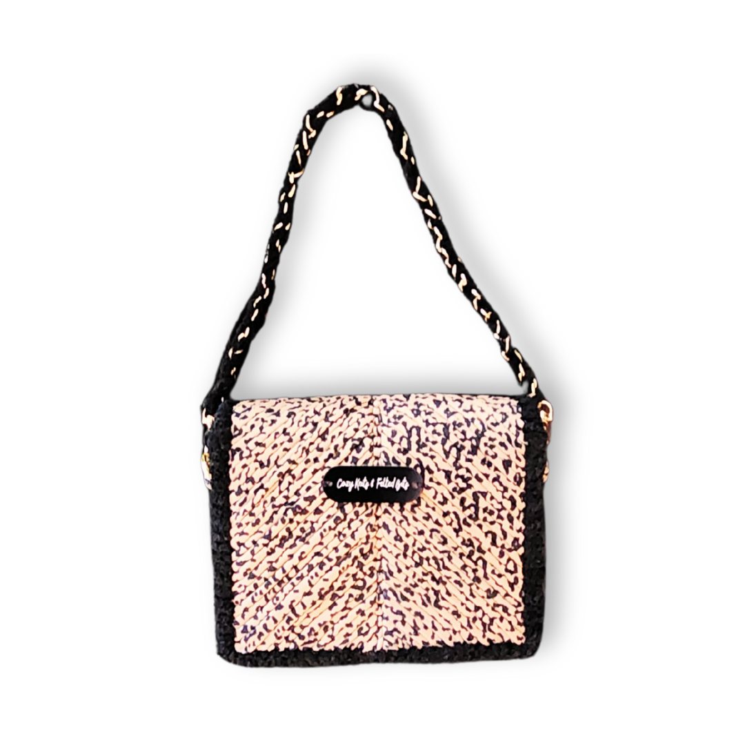 A small, handmade embroidered evening clutch in Leopard Print yarn, featuring a black chenille border and a black and gold woven chain strap hanging above the bag.