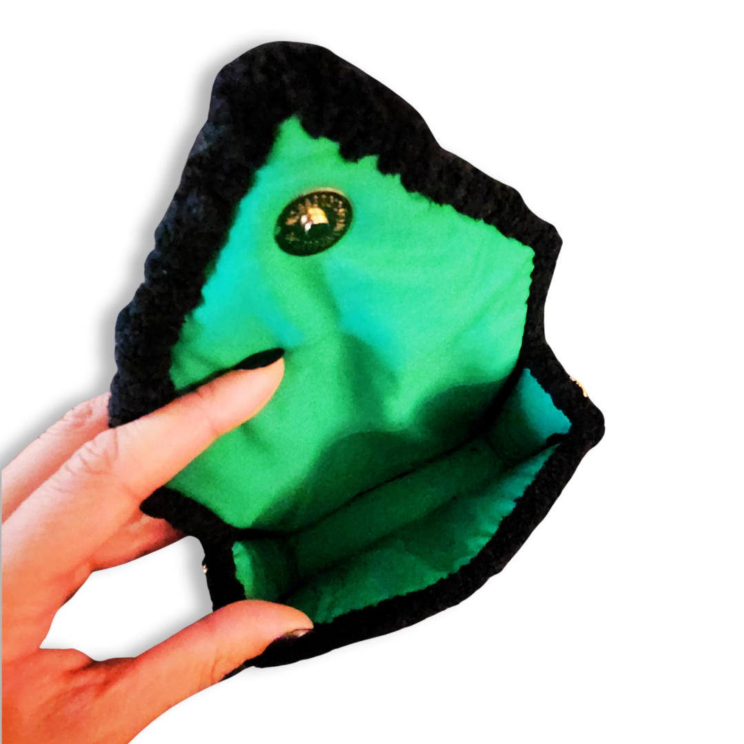 A hand holds the open clutch, showing the bright neon green lining, the round gold magnetic clasp, and the plush black chenille interior trim.