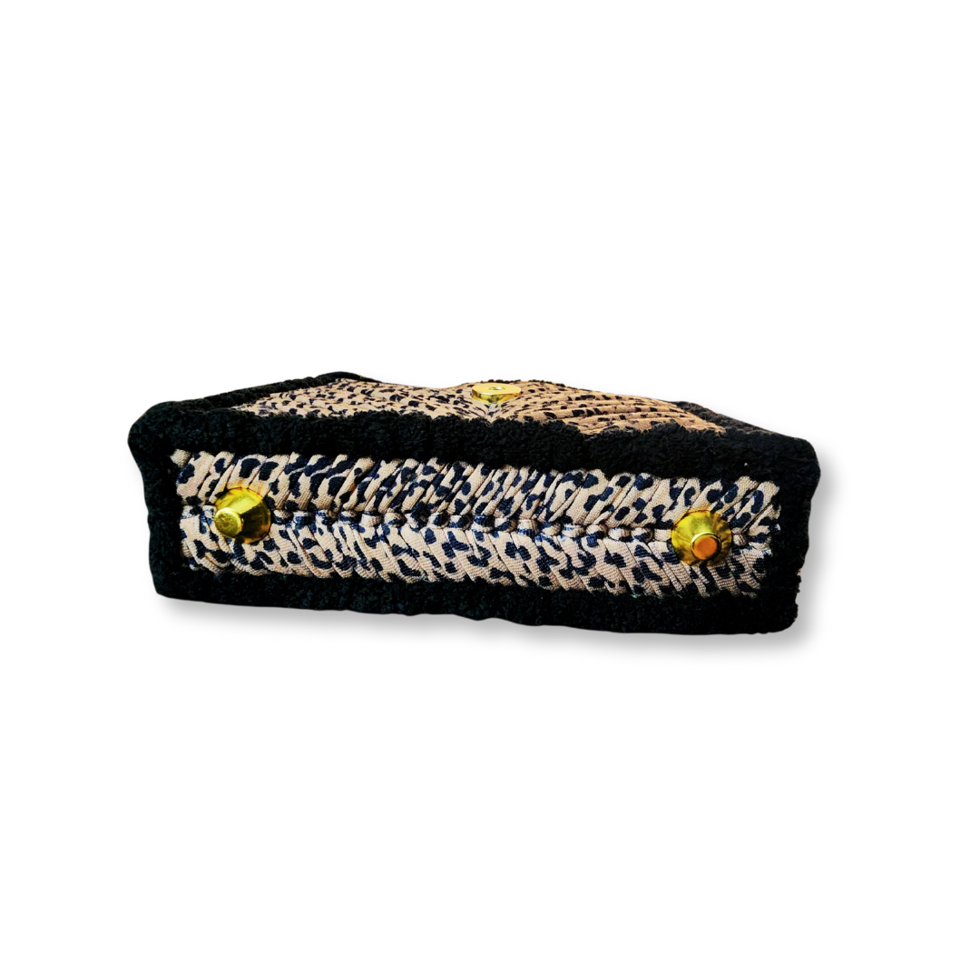 A side profile of the structured clutch, showing its depth and the small gold purse feet on the bottom, with the black chenille sides.