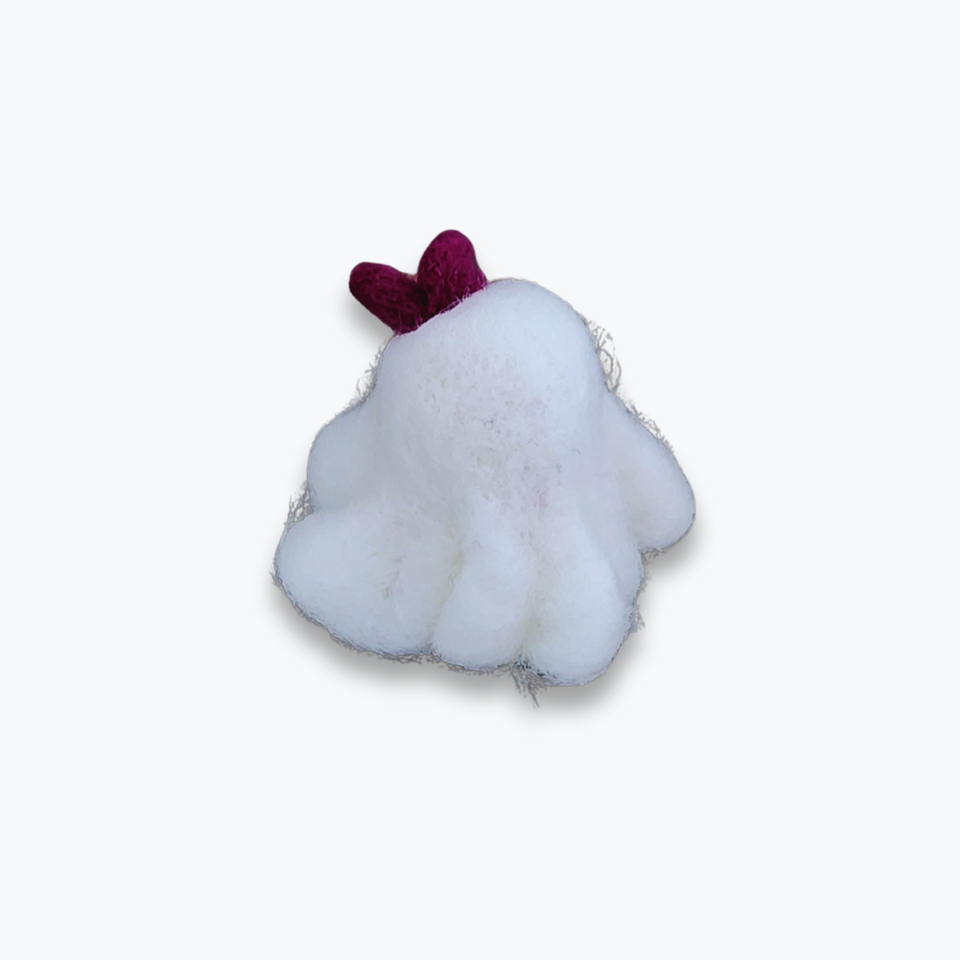 A small handmade felted ghost figurine with a purple bow, a cute smiling mouth, and pink cheeks, viewed from a high angle against a plain white background.