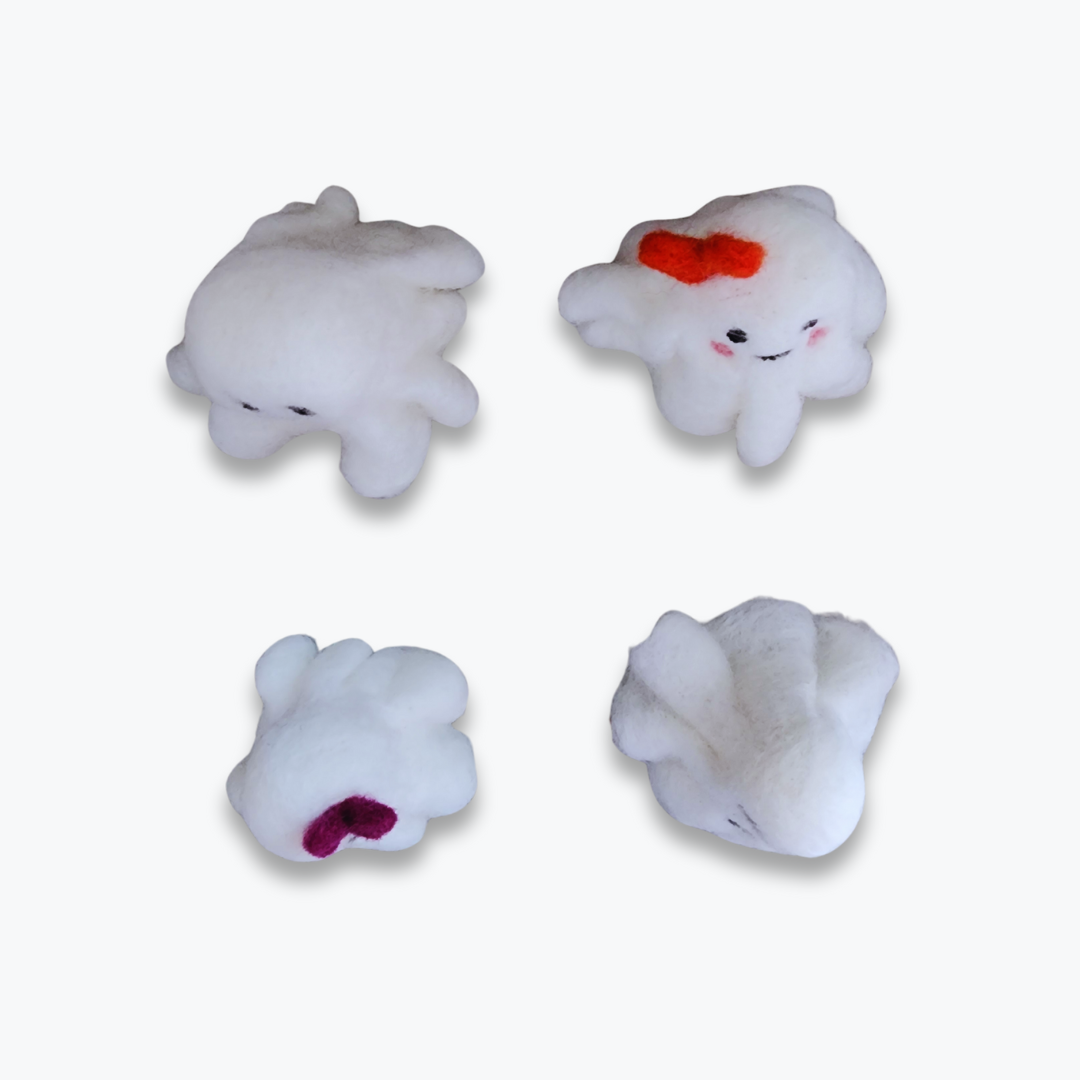 An overhead view of four handmade felted ghost figurines, showing their various features: a plain spooky face, a cute face with a red heart bow, a cute face with a purple bow, and a plain grinning face, all against a white background.