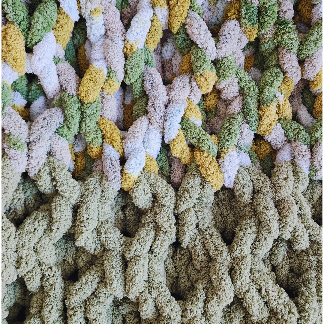 A close-up overhead view of a handmade hand-crocheted blanket, showing the textured honeycomb stitch pattern in a solid light green, transitioning to a multicolored section with green, yellow, and white yarn.