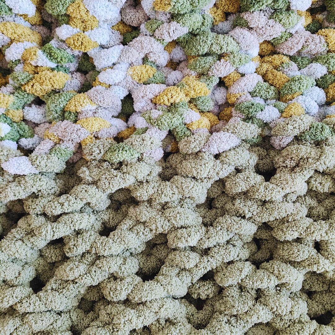 A close-up overhead view of a handmade hand-crocheted blanket, showing the textured pearled side of a honeycomb stitch pattern in a solid light green, transitioning to a multicolored section with green, yellow, and white yarn.