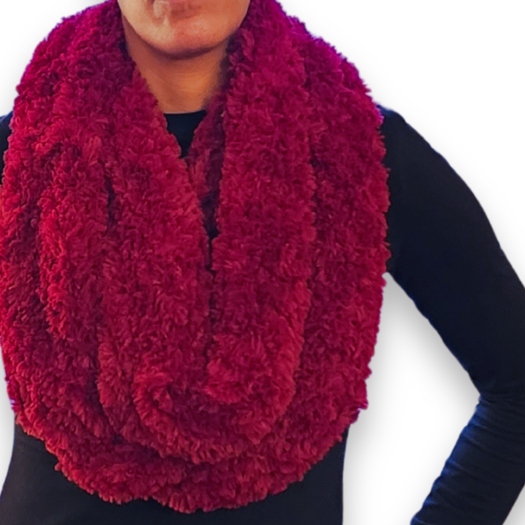 A person models a wide, plush maroon (deep red) faux fur infinity scarf, worn in a double loop around the neck.