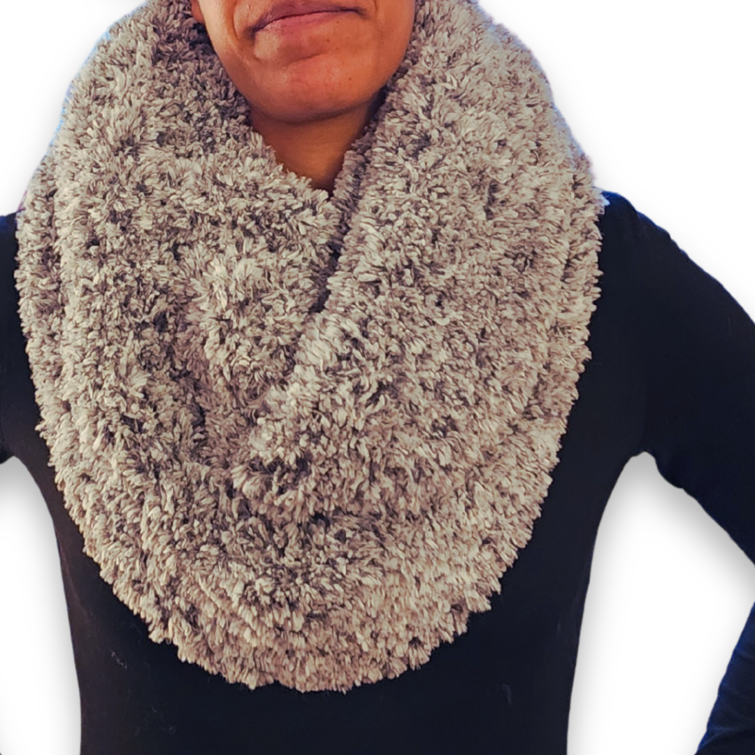 A person models a wide, cozy stone (light gray/taupe) faux fur infinity scarf, looped once around the neck, highlighting the plush texture.