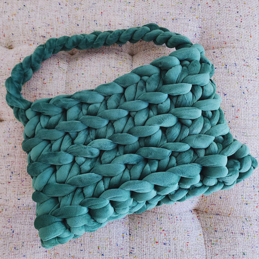 An overhead view looking into a large handmade ribbed shoulder bag in forest green velvet, showing the braided handle and the woven texture of the bag's interior, resting on an upholstered surface.