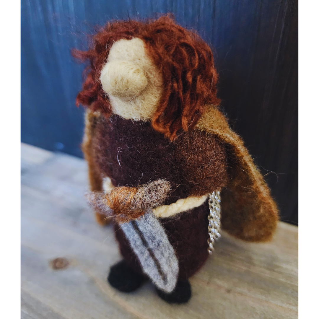 Close-up of a needle-felted Aragorn figure in dark clothing and a brown cloak, holding his sword.